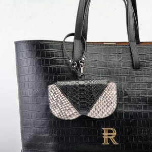 May include: Black tote bag with a crocodile texture, featuring a small, attached pouch with a snakeskin pattern in black and white. The bag has a gold-colored letter "R" on the front.