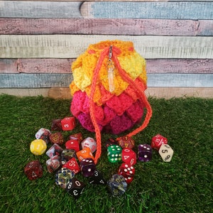 May include: A crocheted dice bag with a rainbow color pattern, filled with colorful dice. The bag has a drawstring closure and a crystal charm.
