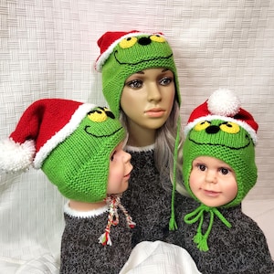 May include: Three green knit hats with a Grinch face design. Each hat has a red brim and a white pom-pom or trim. The hats are on mannequins, and the hats are a festive holiday accessory.