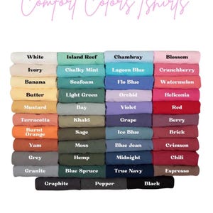 May include: A collection of folded t-shirts arranged in a grid, labeled Comfort Colors Tshirts. The shirts are displayed in various colors including white, ivory, banana, butter, mustard, terracotta, orange, yam, grey, granite, and black.