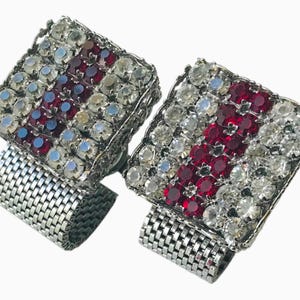 May include: Pair of square cufflinks with a silver mesh band. The square tops are encrusted with clear and red gemstones arranged in a striped pattern. The gemstones are set in a silver metal frame.