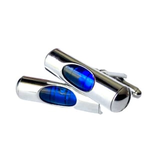 May include: A pair of silver cufflinks shaped like a level with a blue bubble in the center.