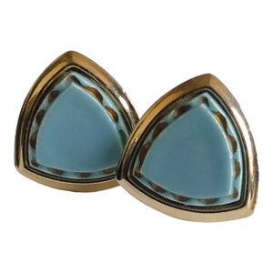 May include: A pair of gold tone earrings with a light blue triangular shaped stone set in the center. The stone is surrounded by a gold tone border.