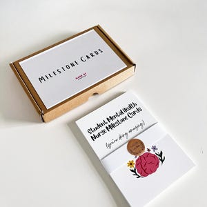 K&ouml;nnte beinhalten: Ein Set Meilensteinkarten f&uuml;r Studenten der psychischen Gesundheitspflege. Die Karten sind wei&szlig; mit Text und einer Gehirngrafik. Die Box ist braun mit dem Aufdruck "MILESTONE CARDS" auf dem Deckel.