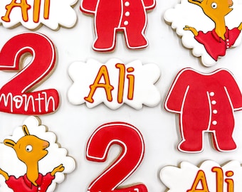 Puede incluir: Un conjunto de nueve galletas de azúcar decoradas. Las galletas están decoradas con glaseado rojo, blanco y amarillo. Las galletas presentan el nombre "Ali", el número "2" y las palabras "mes". Algunas galletas presentan una llama de dibujos animados y un personaje de dibujos animados que lleva un mono rojo.