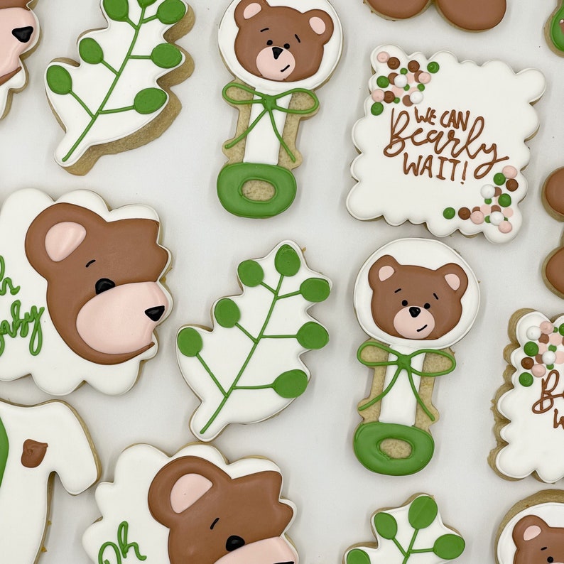 May include: A set of nine decorated sugar cookies featuring a bear theme. The cookies are decorated with brown bears, green leaves, and the text "We can bearly wait!"