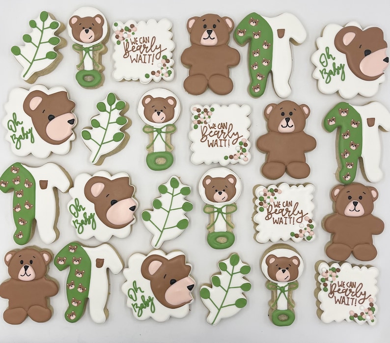 May include: A set of 16 decorated sugar cookies featuring a bear theme. The cookies are decorated with green and brown icing and feature various designs including bears, leaves, and the text "We can bearly wait!" and "Oh baby".