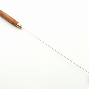 Puede incluir: Una varilla de madera con una punta de latón y una bola de madera en el extremo. La varilla mide aproximadamente 30 cm de largo.