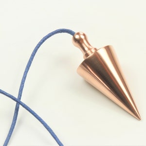 Op de afbeelding: Een koperkleurig slinger met een puntige punt en een ronde knop aan de bovenkant. De slinger is bevestigd aan een blauw koord.