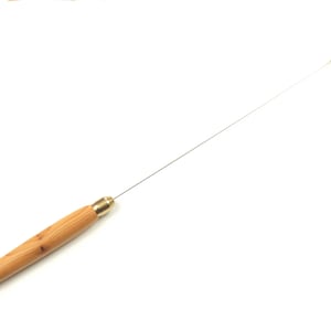 Puede incluir: Una herramienta de madera con una aguja de metal larga y delgada y un mango de madera. La aguja está unida a un anillo de madera en el otro extremo.