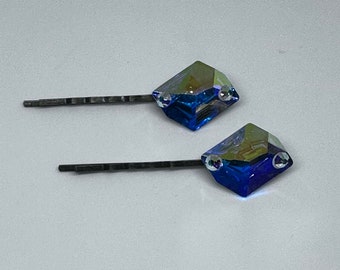 Puede incluir: Dos horquillas plateadas con detalles de cristal azul iridiscente. Los cristales son de forma cuadrada y tienen un diseño facetado.