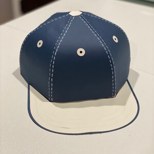May include: A navy blue baseball cap with a white brim and white stitching. The cap has two white eyelets on the crown.