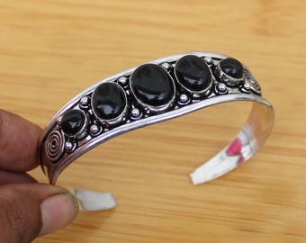 May include: Silver-toned cuff bracelet featuring six oval and round black gemstones. The bracelet has a decorative edge and a spiral design on one end. The open design allows for easy wear.