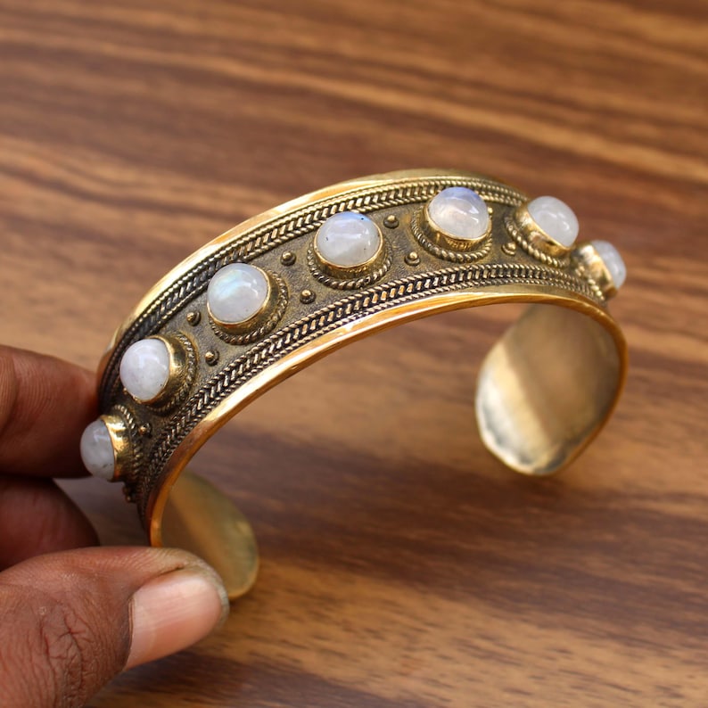 May include: A gold-toned cuff bracelet with a row of round, white gemstones. The bracelet has a textured design along the top edge and is open at the bottom. The gemstones are set in individual bezels.