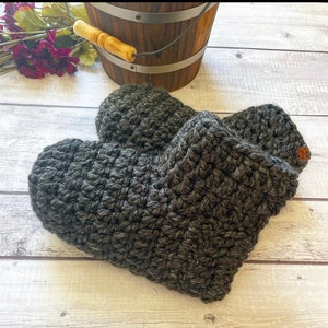 May include: A pair of gray crocheted slippers. The slippers are made with a chunky yarn and have a simple, classic design.