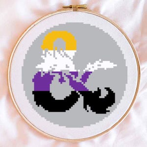 May include: A cross-stitch pattern of the Dungeons and Dragons symbol, with the colors of the non-binary pride flag. The symbol is a stylized 'D' and '20' intertwined, with the colors yellow, white, purple, and black.