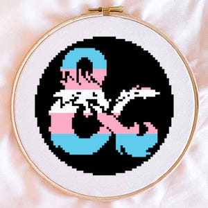 May include: A black and white Dungeons and Dragons symbol with a transgender pride flag color scheme. The symbol is a stylized 'D&D' logo with a blue, pink, and white color scheme.