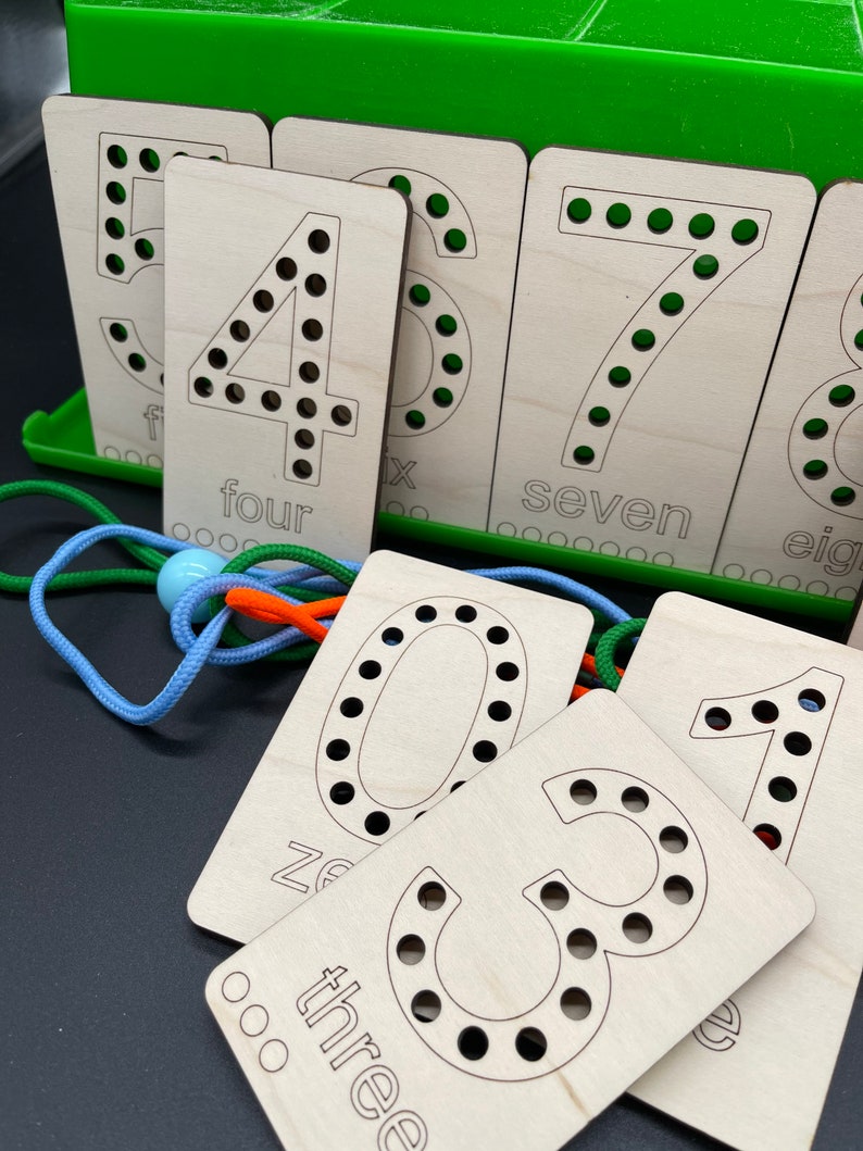May include: Wooden cards with numbers 0 through 8, each with holes for lacing. The cards are arranged in a row, with the numbers in order. The cards are light brown and have black numbers and text. The text on the cards reads "zero", "one", "two", "three", "four", "five", "six", "seven", and "eight".