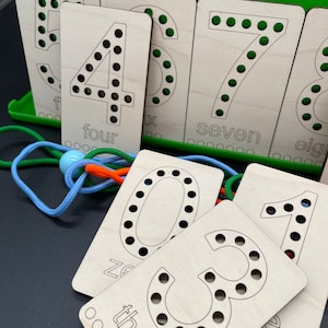 May include: Wooden cards with numbers 1 through 8, with holes for threading string. The cards are labeled with the number and the word for the number. The cards are on a green surface.