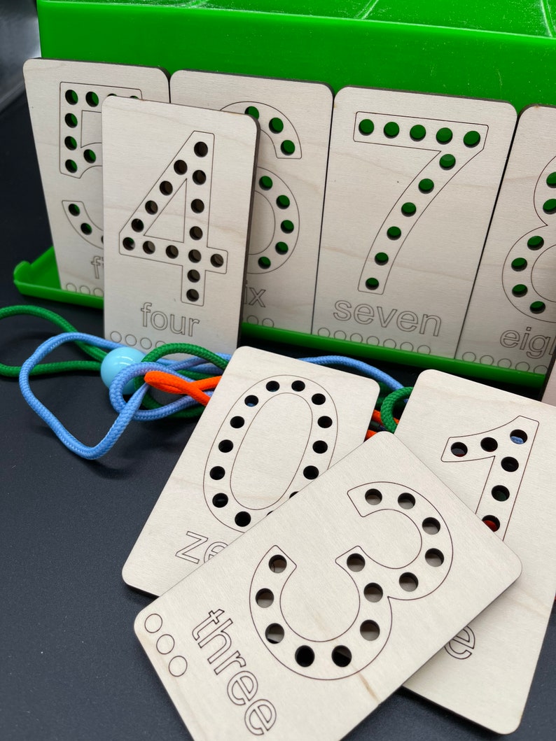 May include: Wooden cards with numbers 1 through 8, with holes for threading string. The cards are labeled with the number and the word for the number. The cards are on a green surface.