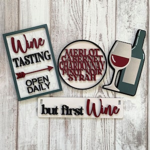 May include: Wooden signs with a wine theme. One sign says "Wine Tasting Open Daily" with an arrow pointing to the right. Another sign says "but first Wine". A third sign has a circle with the words "Merlot, Cabernet, Chardonnay, Pinot Noir, Syrah" written on it. A fourth sign has a wine glass and a bottle of wine.