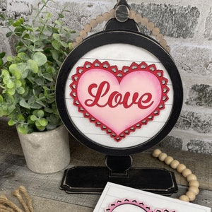 Pu&ograve; includere: Un globo terrestre in legno bianco e nero con un cuore ritagliato rosa e rosso su cui &egrave; scritto "Love". Il globo &egrave; su un piedistallo nero.
