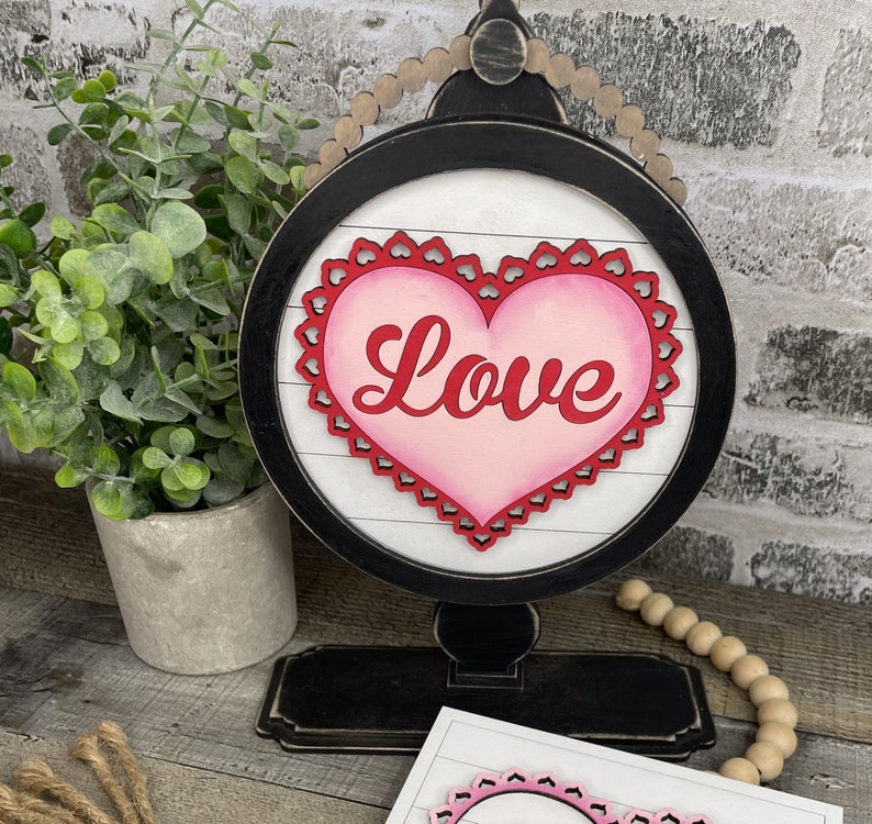 Pu&ograve; includere: Un globo terrestre in legno bianco e nero con un cuore ritagliato rosa e rosso su cui &egrave; scritto "Love". Il globo &egrave; su un piedistallo nero.