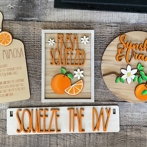 May include: A set of five wooden signs with orange and white accents. The signs feature the text "Classic Mimosa", "Fresh Squeezed", "Sunshine & Oranges", and "Squeeze the Day".