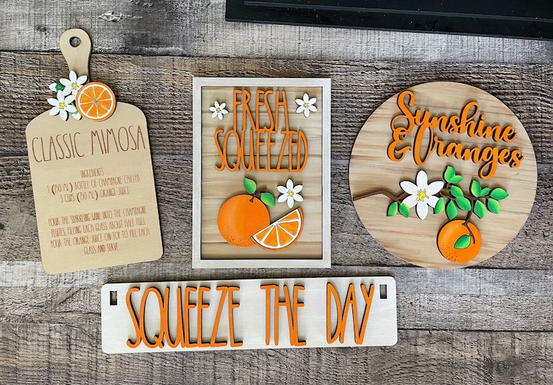 May include: A set of five wooden signs with orange and white accents. The signs feature the text "Classic Mimosa", "Fresh Squeezed", "Sunshine & Oranges", and "Squeeze the Day".