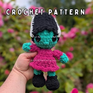 May include: A crochet pattern document featuring a teal-skinned doll with black hair, white streaks, and a magenta dress. The text CROCHET PATTERN is displayed at the top, and the text HANDMADEBYNIKELLE is visible on the doll's torso.