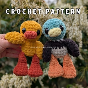 May include: Two handmade crochet ducklings. One is yellow with orange feet and beak, the other is blue, black, and gray with orange feet and a yellow beak. The text "CROCHET PATTERN" is at the top of the image, and the text "@HANDMADEBYNIKELLE" is at the bottom.