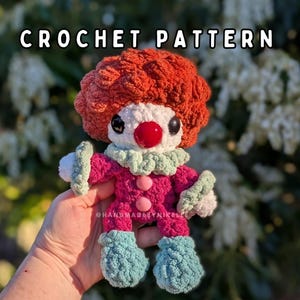 May include: A crocheted clown doll with a red wig, white face, and red nose. The clown is dressed in a pink outfit with a green collar and blue shoes. The text "CROCHET PATTERN" is displayed at the top of the image.