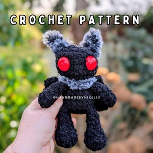 May include: A black crochet creature with red eyes and gray accents. The plushie has a furry collar and ears. The text "CROCHET PATTERN" is at the top of the image. The creator's handle, @HANDMADEBYNIKELLE, is at the bottom.