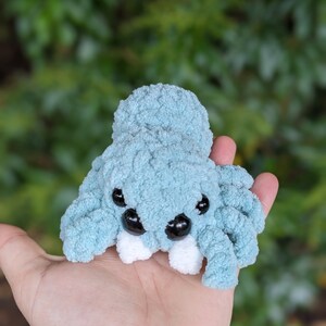 Puede incluir: Un juguete de peluche de ara&ntilde;a de crochet azul claro con dientes blancos y ojos negros.