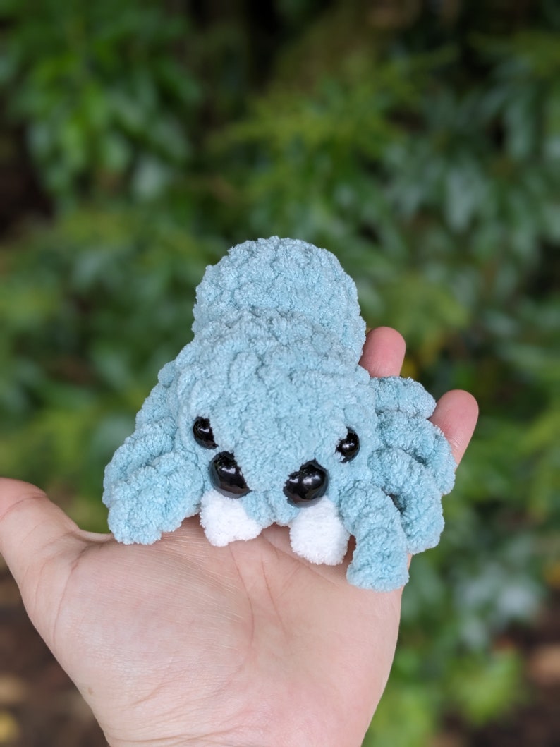 Puede incluir: Un juguete de peluche de ara&ntilde;a de crochet azul claro con dientes blancos y ojos negros.