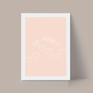 May include: A white framed print with a pink background and white text that says "BE MINE?" with a row of white hearts underneath.