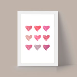 May include: A white framed print with nine pink, red, and peach hearts painted in a gradient pattern.