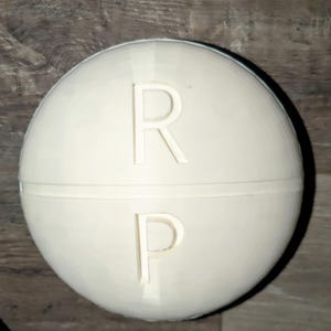 May include: White pill container with the letters "R" and "P" printed on it.