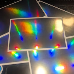 May include: A set of iridescent holographic stickers with a rainbow effect. The stickers are rectangular and have a glossy finish.