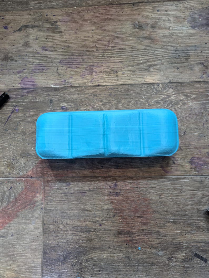 May include: A light blue plastic storage case with four compartments. The case is empty and has a smooth, slightly textured surface.