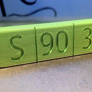 May include: A green block with the letters "S 90 3" carved into it.