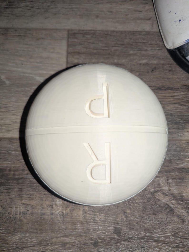 May include: White pill box with a round shape and a hinged lid. The top of the box has the letters "D" and "R" embossed on it.
