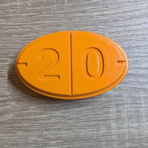 May include: An orange, oval-shaped object with the number "20" prominently displayed. The number is divided into two sections, with a horizontal line on each side. The object is on a wooden surface.
