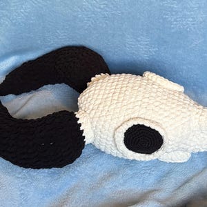 May include: A crochet plush toy shaped like a skull with large, curved black horns extending from the sides. The skull portion is white with a textured, knotted yarn surface, while the eye sockets are filled with solid black circular crochet.
