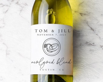 May include: A clear wine bottle with a white label featuring the names "TOM & JILL" and the date "NOVEMBER 7, 2023". The label also includes a ring design and the words "newlywed blend" and "TUSTIN, CA".
