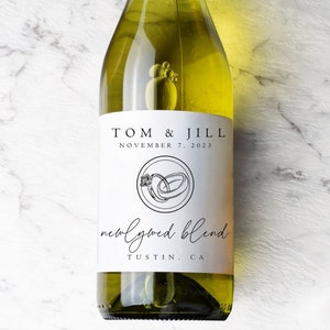 May include: A clear wine bottle with a white label featuring the names "TOM & JILL" and the date "NOVEMBER 7, 2023". The label also includes a ring design and the words "newlywed blend" and "TUSTIN, CA".