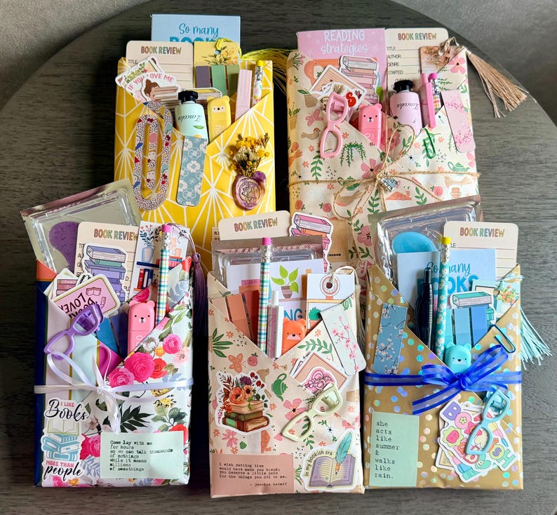May include: Five rectangular gift envelopes wrapped in patterned paper, each containing stationery items like book review cards, pens, stickers, and paper clips. The envelopes feature floral, geometric, and polka dot designs with ribbons.