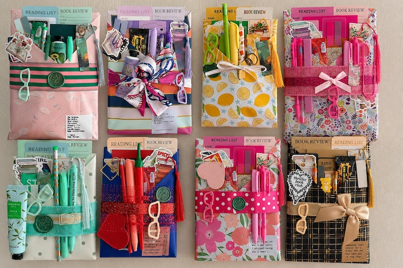 May include: Eight rectangular gift packages arranged in two rows, each wrapped in patterned paper and secured with a ribbon. Each package contains stationery items, pens, reading list cards, and decorative stickers, with some featuring wax seals.