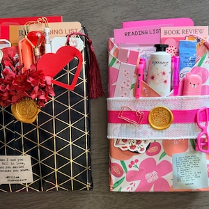 May include: Two wrapped book gifts featuring stationery accessories. The left gift has black and gold geometric paper, a red heart, and a Shakespeare quote. The right gift has pink floral paper, a white bottle, and a pink ribbon with a gold wax seal.