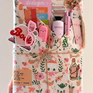 May include: A rectangular gift package wrapped in floral paper featuring birds, houses, and teapots. It contains a reading strategies card, a book review form, a pink bear-shaped highlighter, a pink pen, a pencil, and stickers including a book and a bottle.